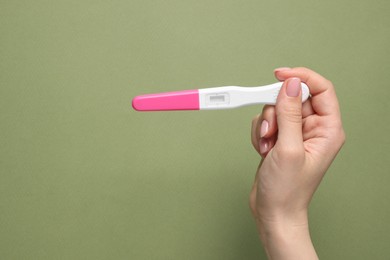 Photo of Woman holding pregnancy test on olive background, top view. Space for text