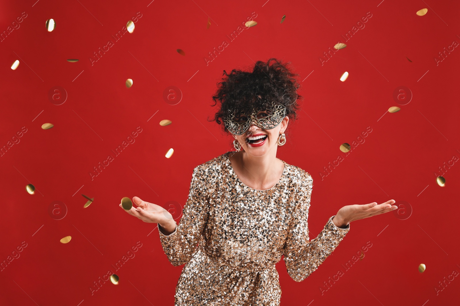 Photo of Happy young woman wearing carnival mask on red background with confetti