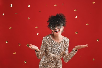 Photo of Happy young woman wearing carnival mask on red background with confetti