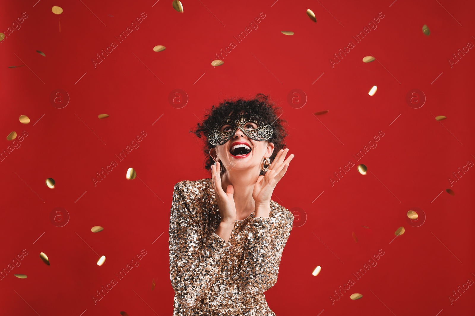 Photo of Happy young woman wearing carnival mask on red background with confetti