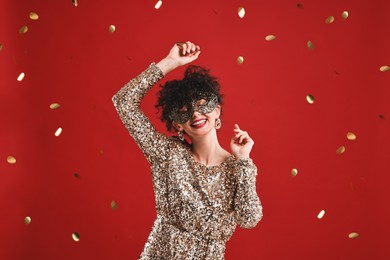 Photo of Happy young woman wearing carnival mask on red background with confetti