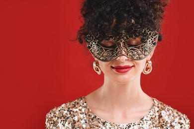 Photo of Beautiful young woman with carnival mask on red background, space for text