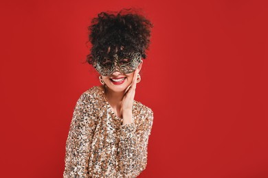 Photo of Smiling young woman wearing carnival mask on red background, space for text