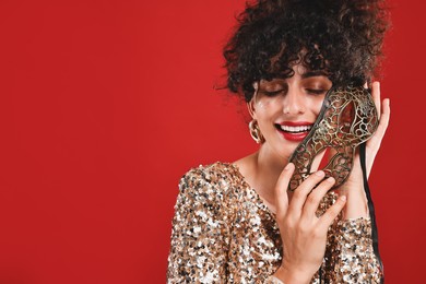 Smiling young woman with carnival mask on red background, space for text