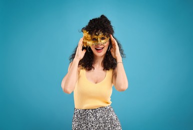 Happy young woman wearing carnival mask on light blue background