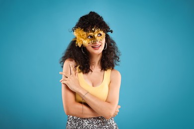 Happy young woman wearing carnival mask on light blue background