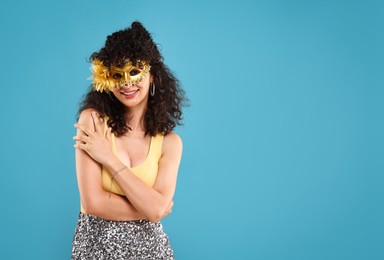 Happy young woman wearing carnival mask on light blue background, space for text