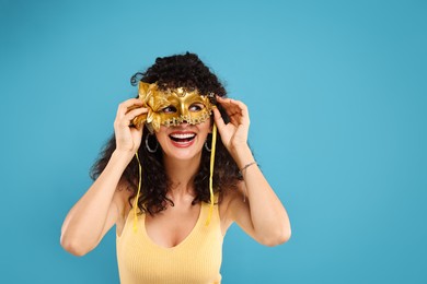 Happy young woman with carnival mask on light blue background, space for text