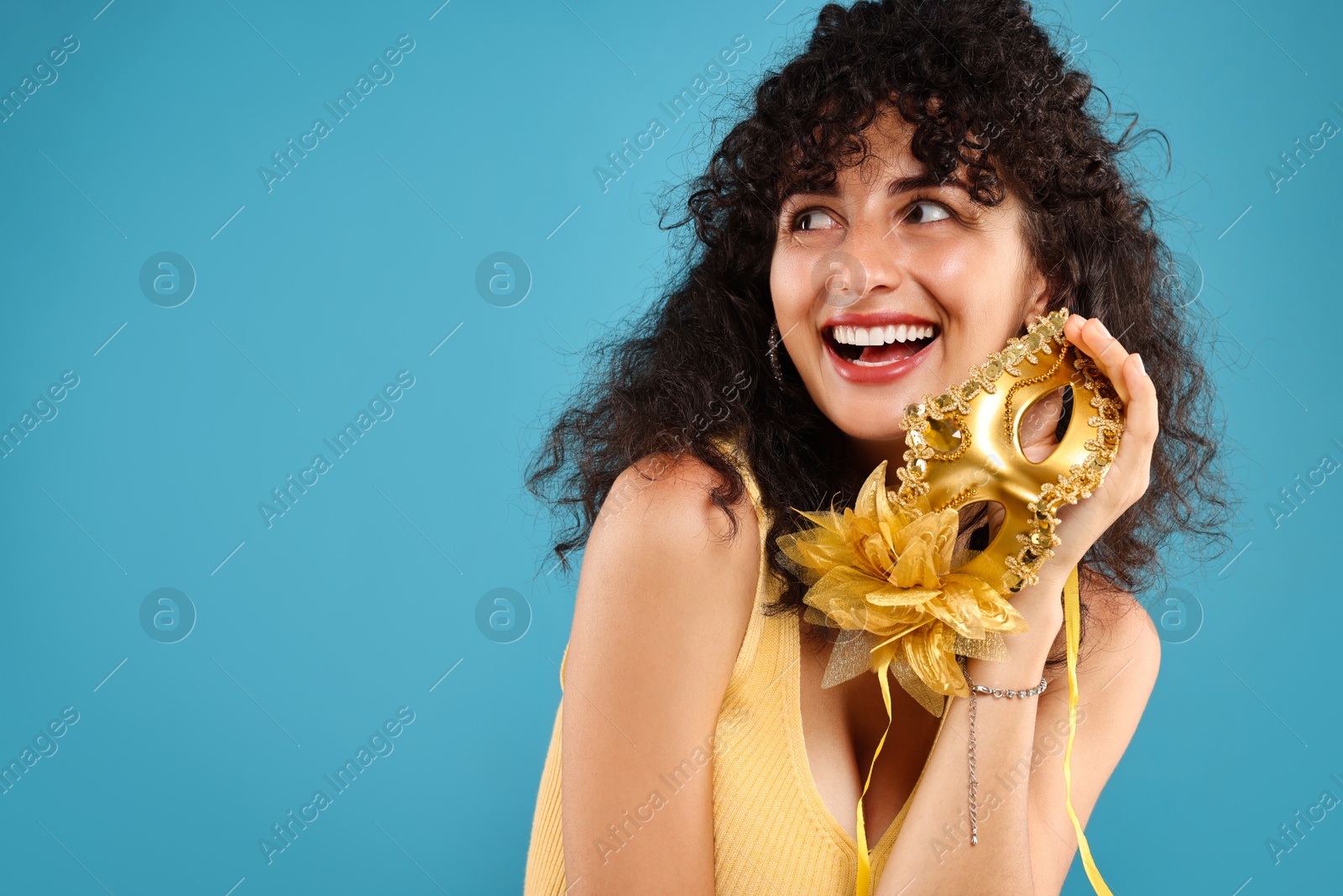 Photo of Happy young woman with carnival mask on light blue background, space for text