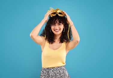 Happy young woman with carnival mask on light blue background