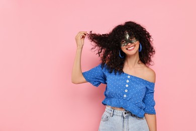 Photo of Happy young woman wearing carnival mask on pink background, space for text