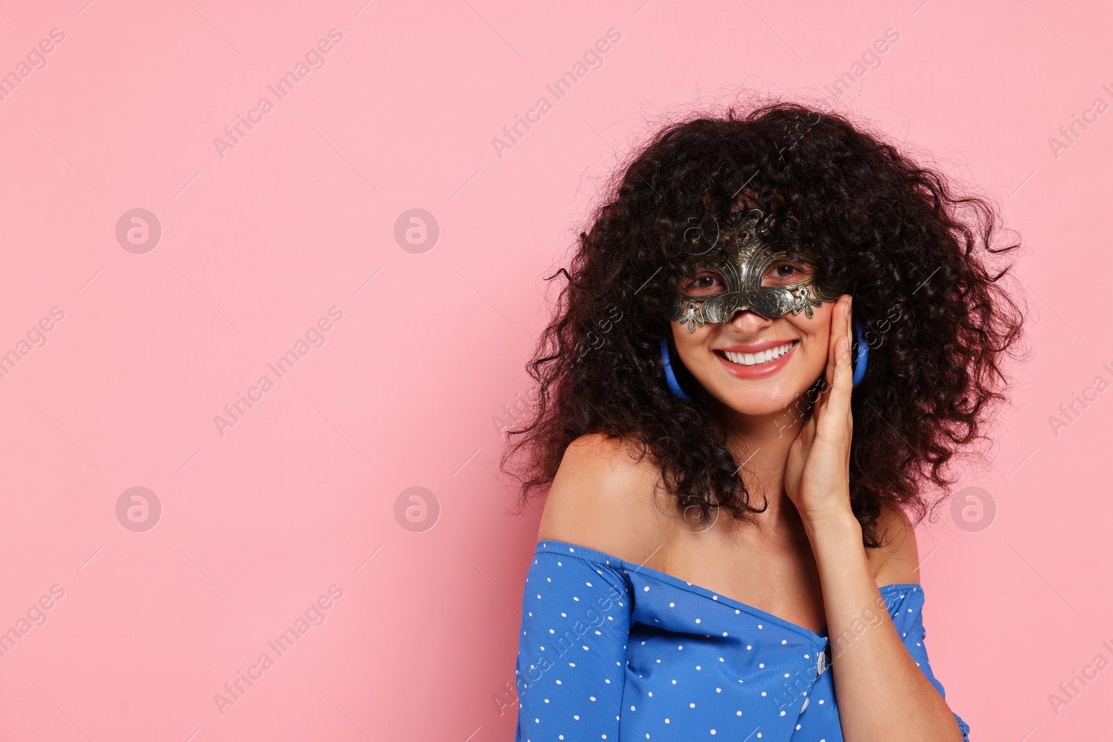 Photo of Happy young woman wearing carnival mask on pink background, space for text