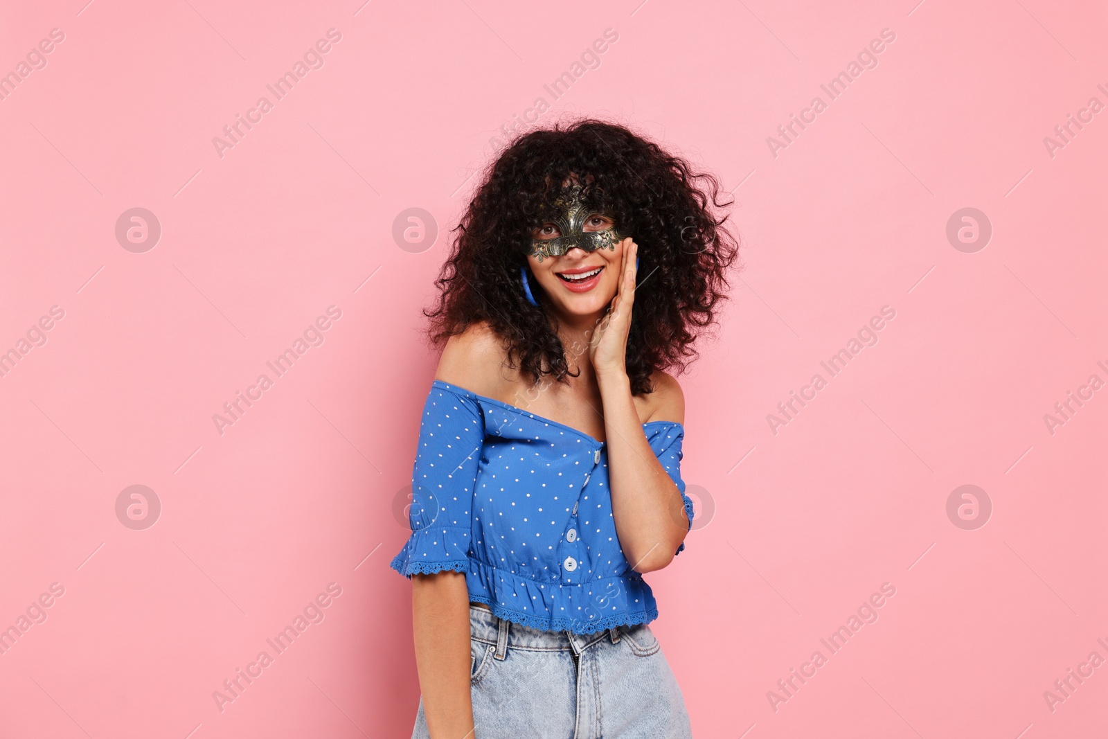 Photo of Happy young woman wearing carnival mask on pink background