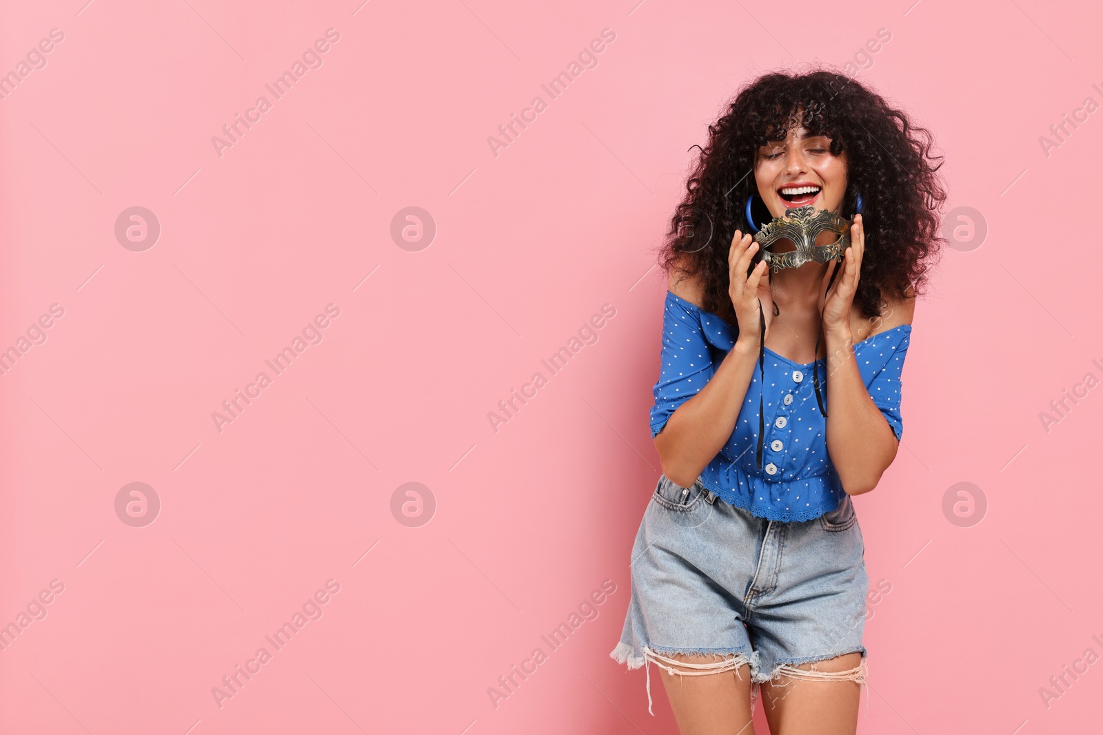 Photo of Smiling young woman with carnival mask on pink background, space for text