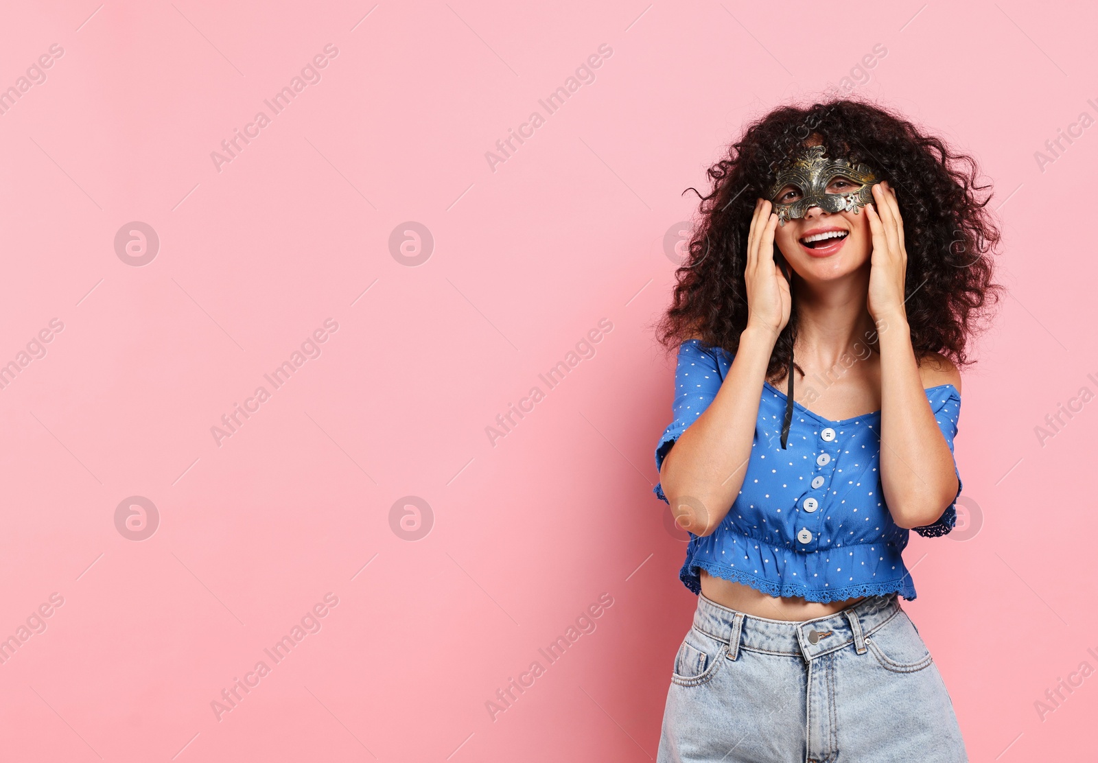 Photo of Happy young woman wearing carnival mask on pink background, space for text