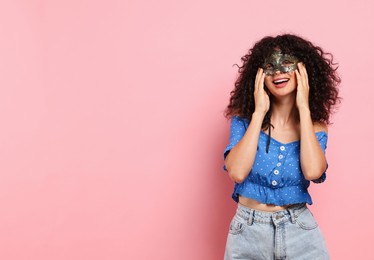 Photo of Happy young woman wearing carnival mask on pink background, space for text