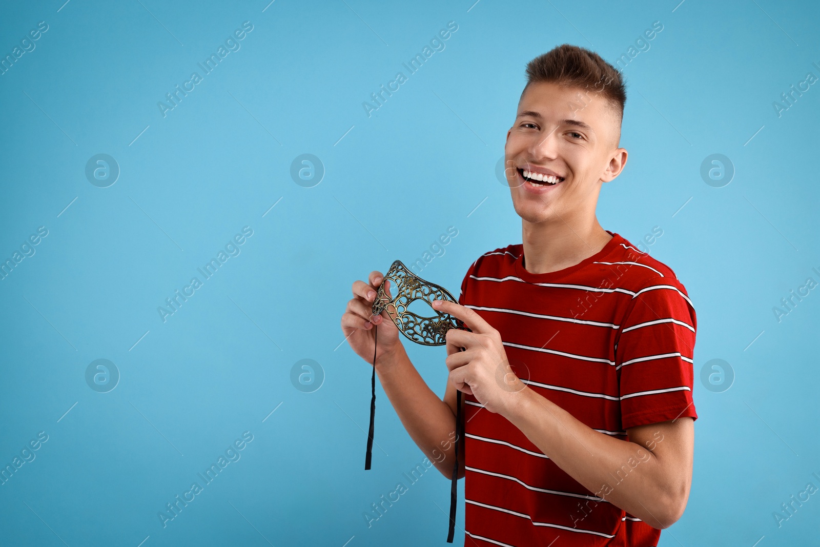 Photo of Charming young man with carnival mask on light blue background. Space for text