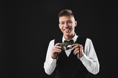 Charming young man with carnival mask on black background. Space for text