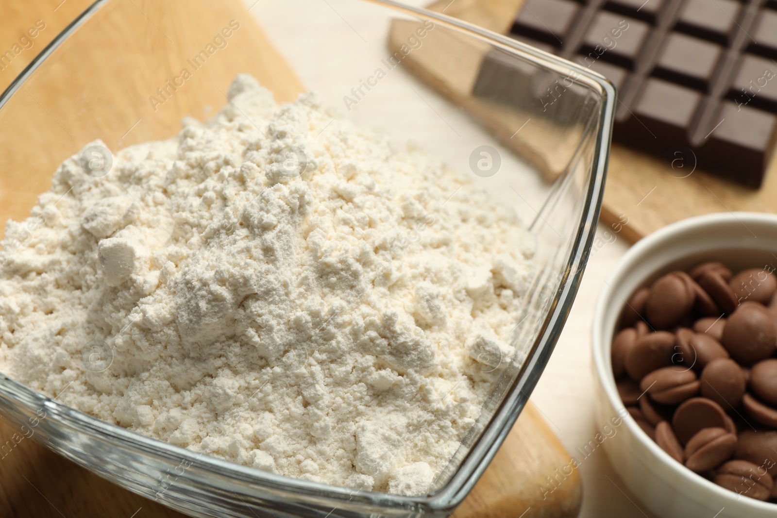 Photo of Flour in bowl and chocolate for making dough on light table, closeup