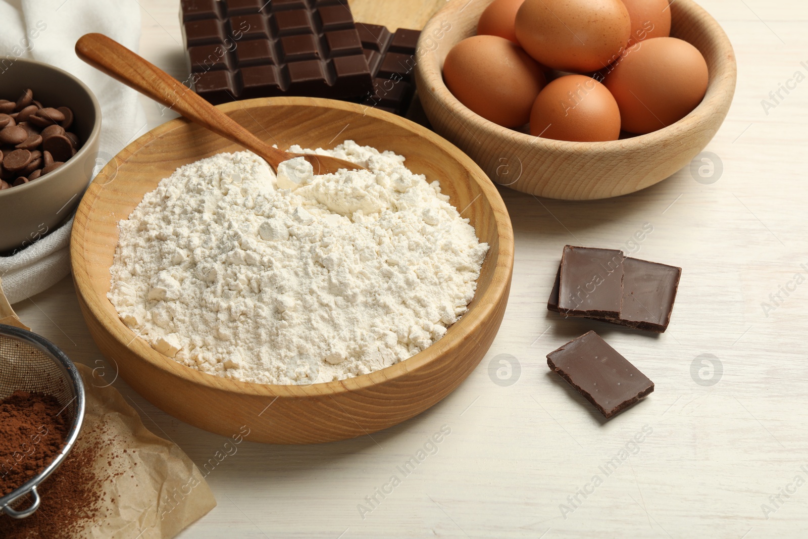 Photo of Flour in bowl and chocolate for making dough on light wooden table, closeup