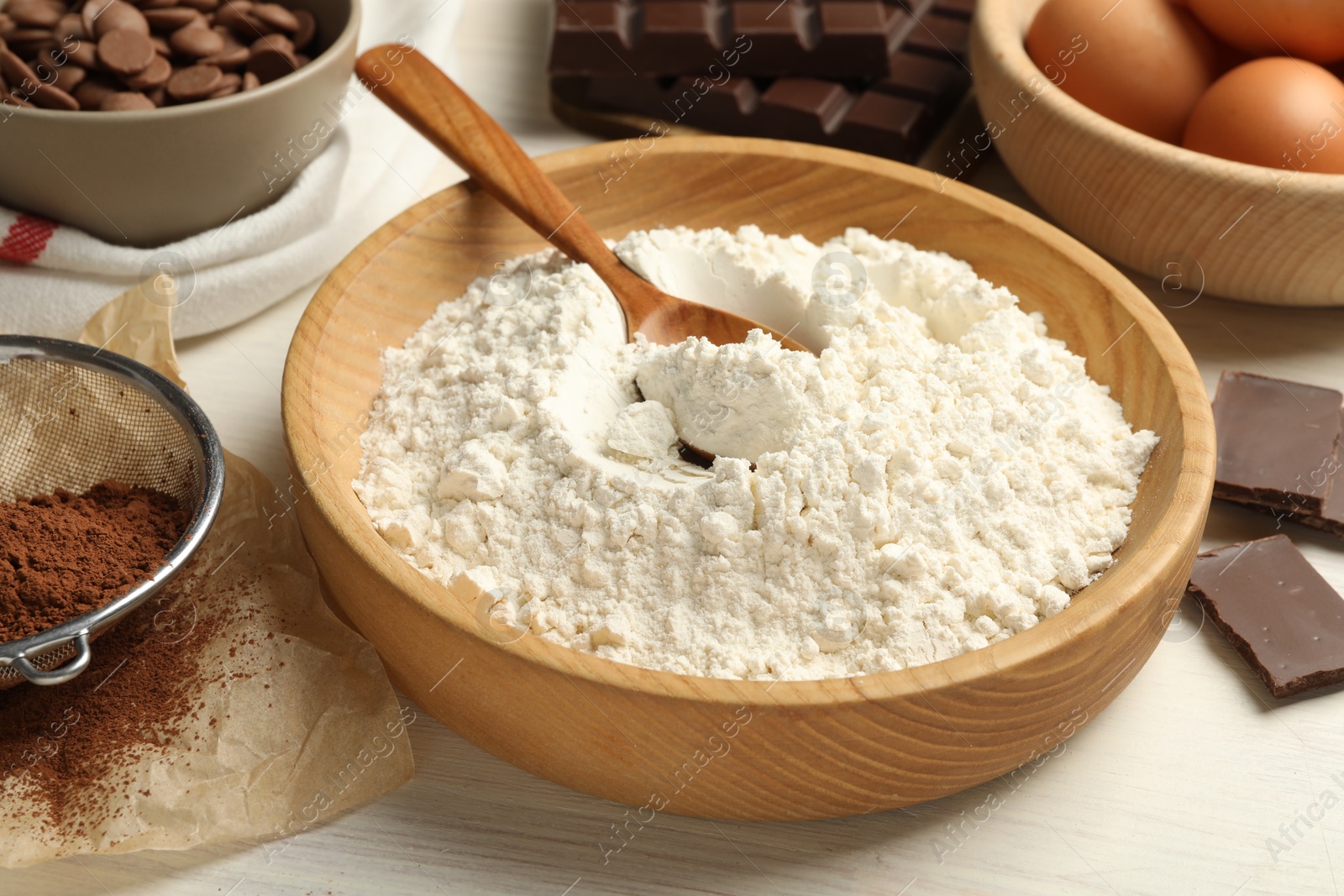 Photo of Flour in bowl and chocolate for making dough on light wooden table, closeup