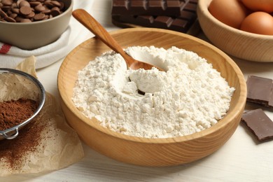 Photo of Flour in bowl and chocolate for making dough on light wooden table, closeup