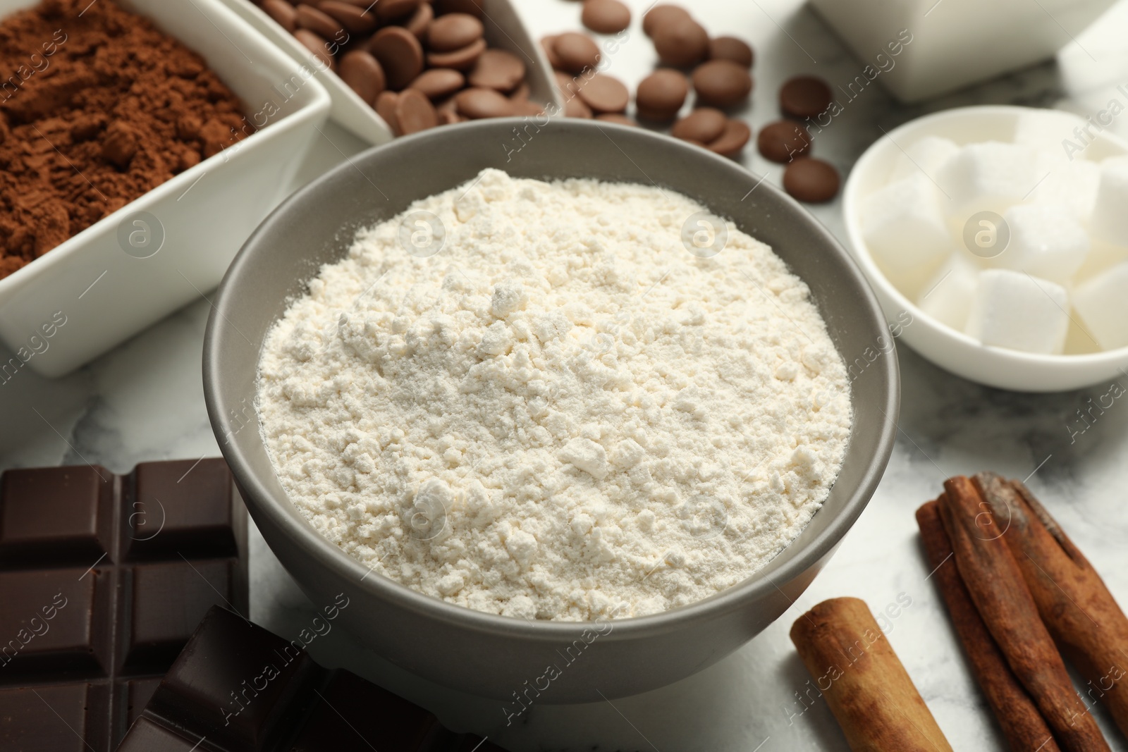 Photo of Flour in bowl and chocolate for making dough on white table, closeup