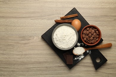 Photo of Flour, chocolate and other ingredients for making dough on wooden table, top view. Space for text