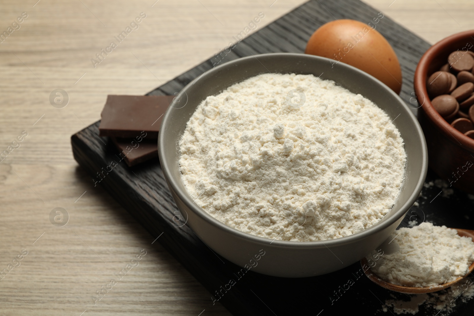 Photo of Flour in bowl, egg and chocolate for making dough on wooden table, closeup