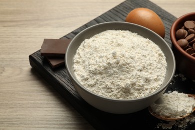 Photo of Flour in bowl, egg and chocolate for making dough on wooden table, closeup