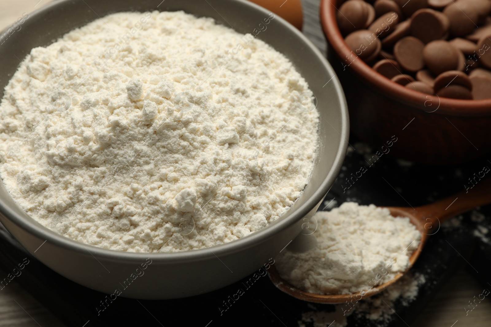 Photo of Flour in bowl and chocolate chips for making dough on table, closeup