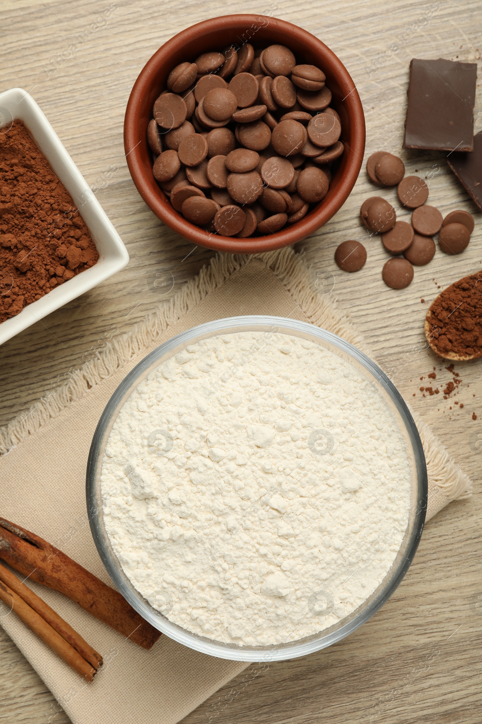 Photo of Flour, chocolate and cocoa for making dough on wooden table, flat lay