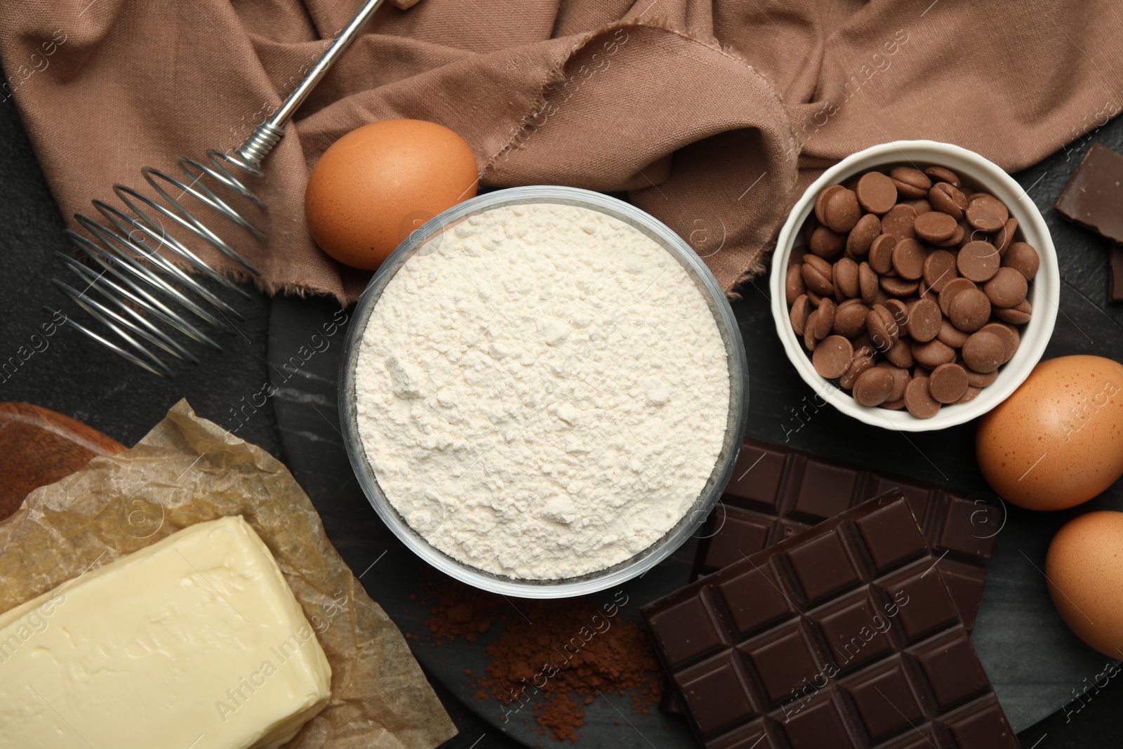 Photo of Flour, chocolate, eggs and butter for making dough on dark table, flat lay