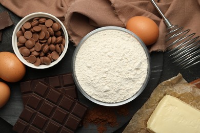 Photo of Flour, chocolate, eggs and butter for making dough on dark table, flat lay