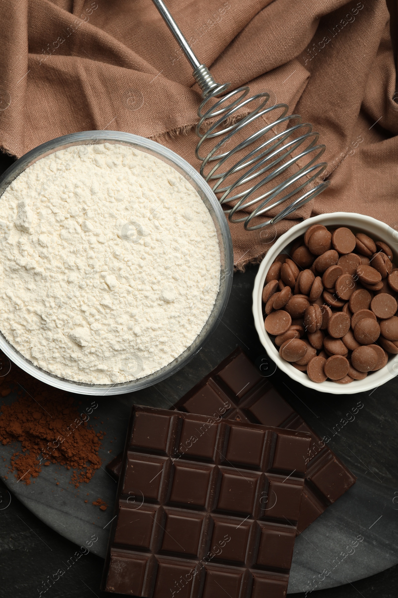 Photo of Flour, chocolate and cocoa for making dough on dark table, flat lay