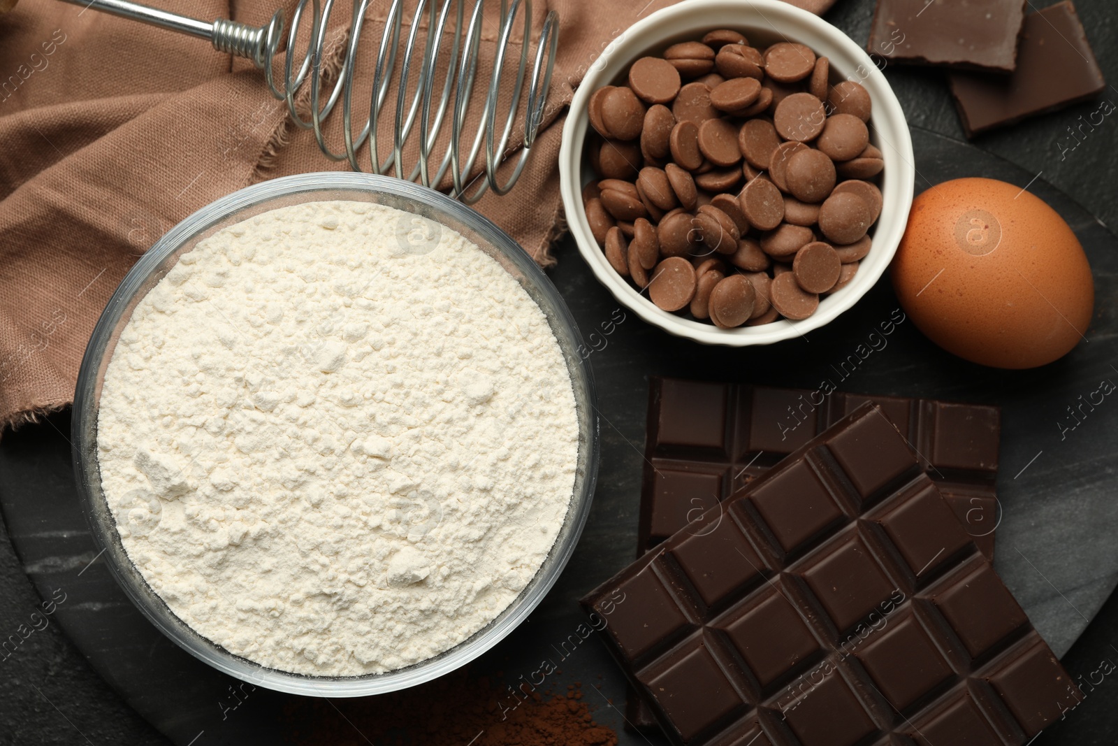 Photo of Flour, chocolate and egg for making dough on dark table, flat lay