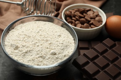 Photo of Flour, chocolate and egg for making dough on dark table, closeup