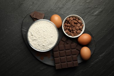 Photo of Flour, chocolate and eggs for making dough on dark textured table, top view