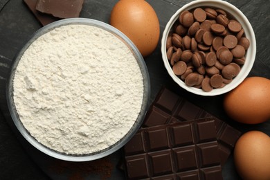 Photo of Flour, chocolate and eggs for making dough on dark table, flat lay