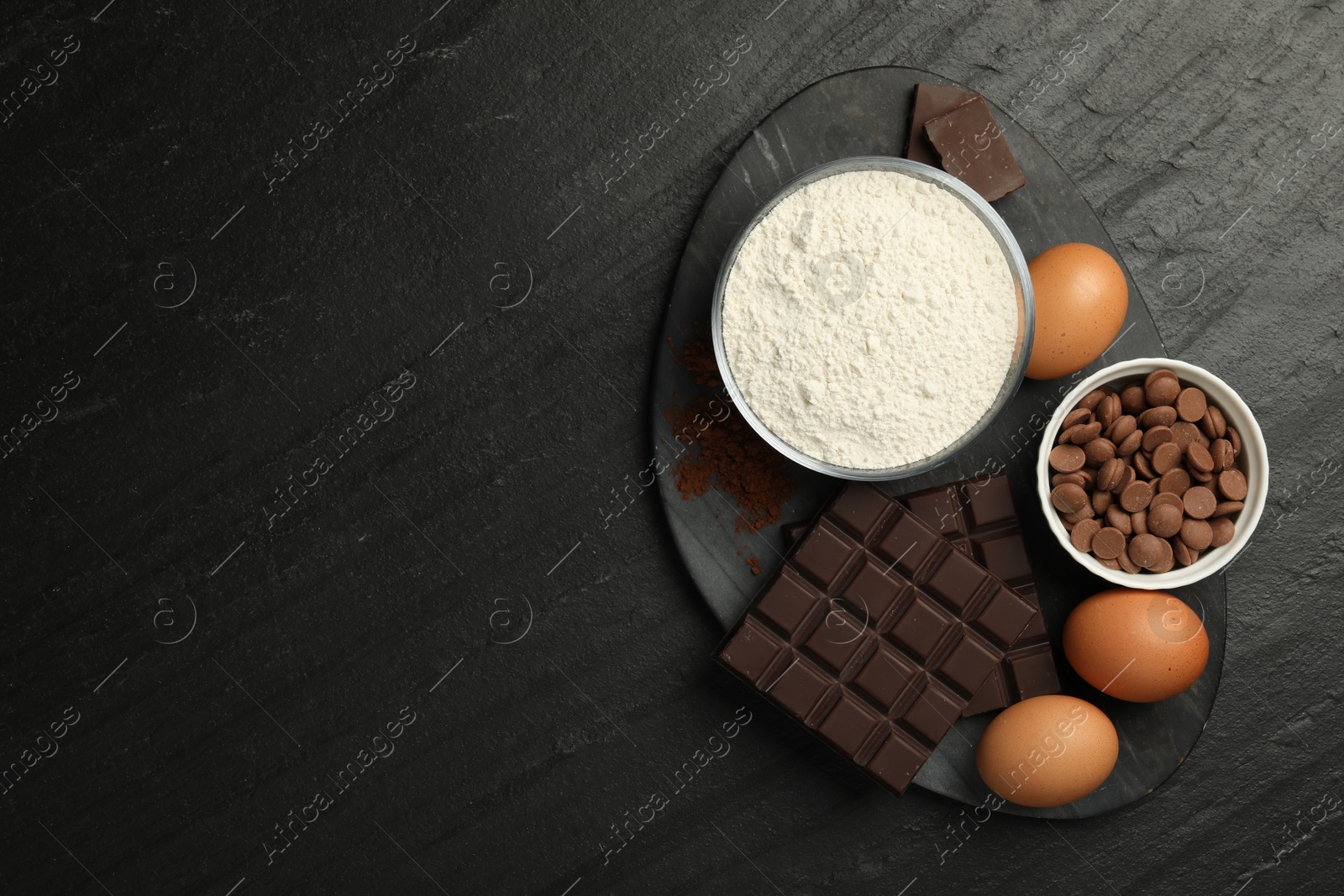 Photo of Flour, chocolate and eggs for making dough on dark textured table, top view. Space for text