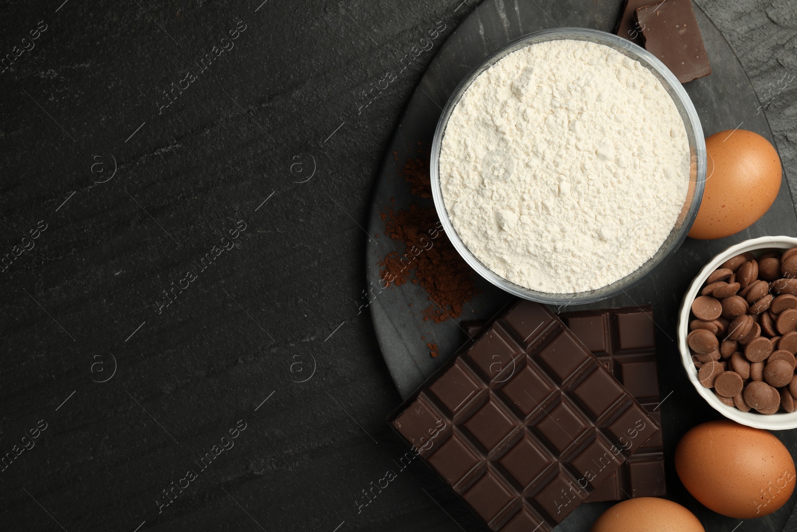 Photo of Flour, chocolate and eggs for making dough on dark textured table, top view. Space for text