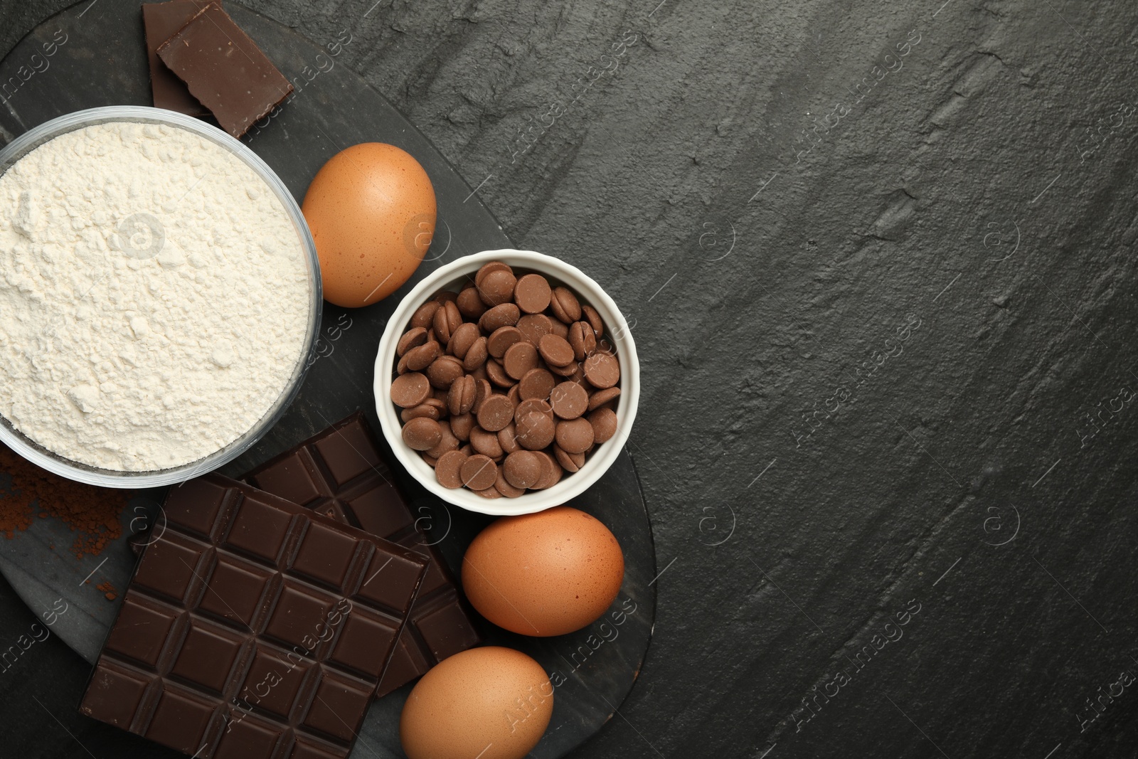 Photo of Flour, chocolate and eggs for making dough on dark textured table, top view. Space for text