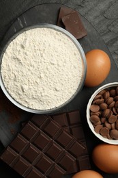 Photo of Flour, chocolate and eggs for making dough on dark textured table, top view