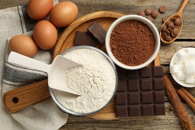 Photo of Flour, chocolate, cocoa and eggs for making dough on wooden table, flat lay