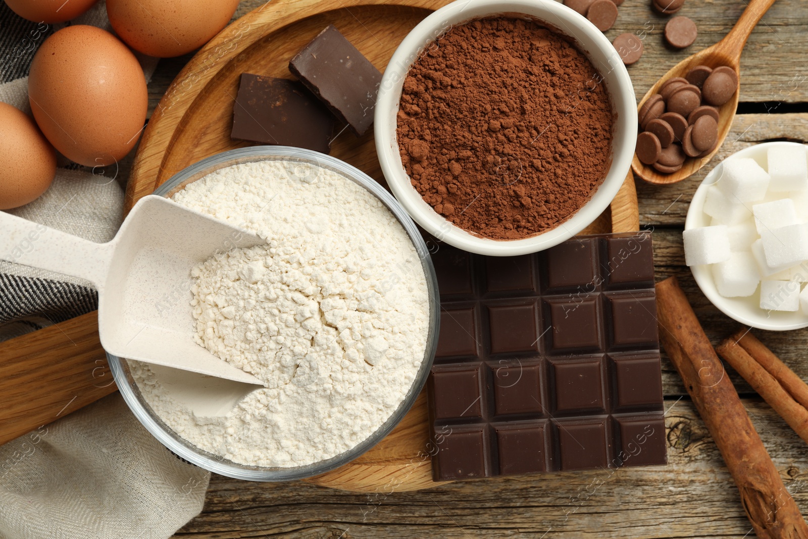 Photo of Flour, chocolate, cocoa and eggs for making dough on wooden table, flat lay