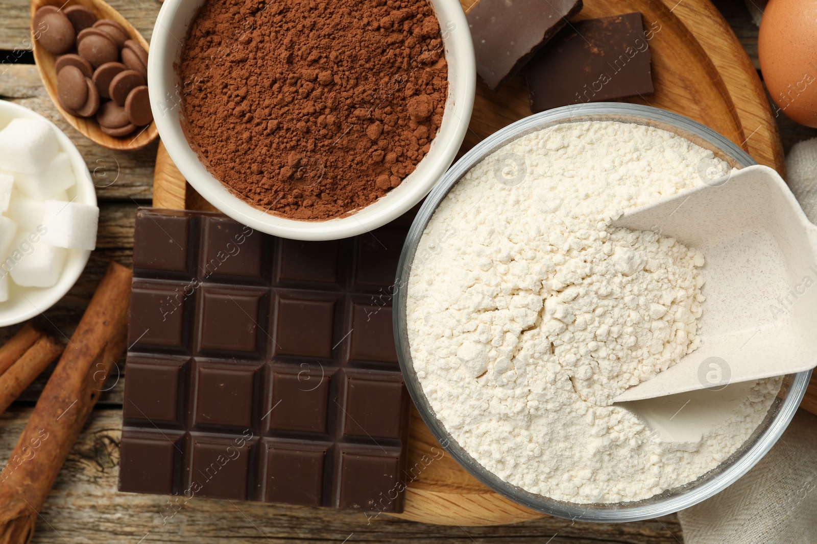 Photo of Flour, chocolate and cocoa for making dough on wooden table, flat lay