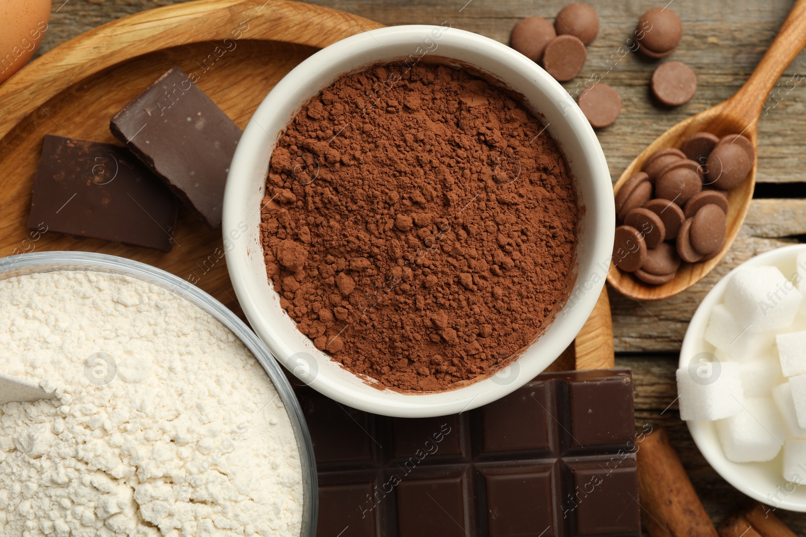 Photo of Flour, chocolate and cocoa for making dough on wooden table, flat lay