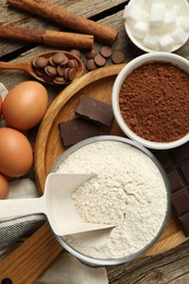 Photo of Flat lay composition with flour, cocoa and other ingredients for making dough on wooden table