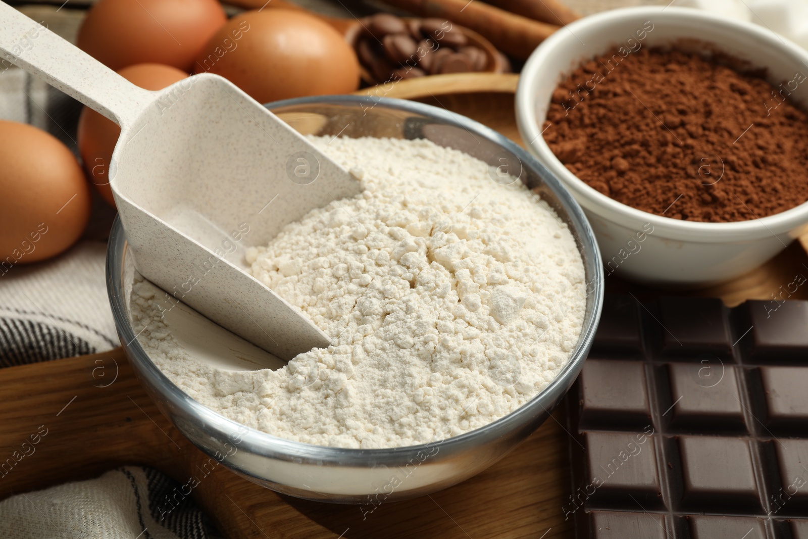 Photo of Flour and scoop in bowl, cocoa and chocolate for making dough on table, closeup