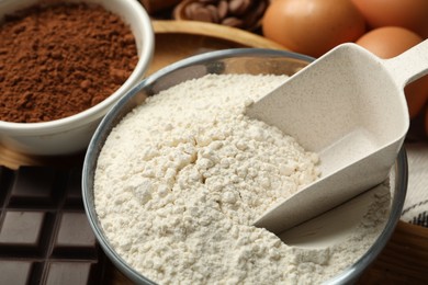 Photo of Flour and scoop in bowl, cocoa and eggs for making dough on table, closeup